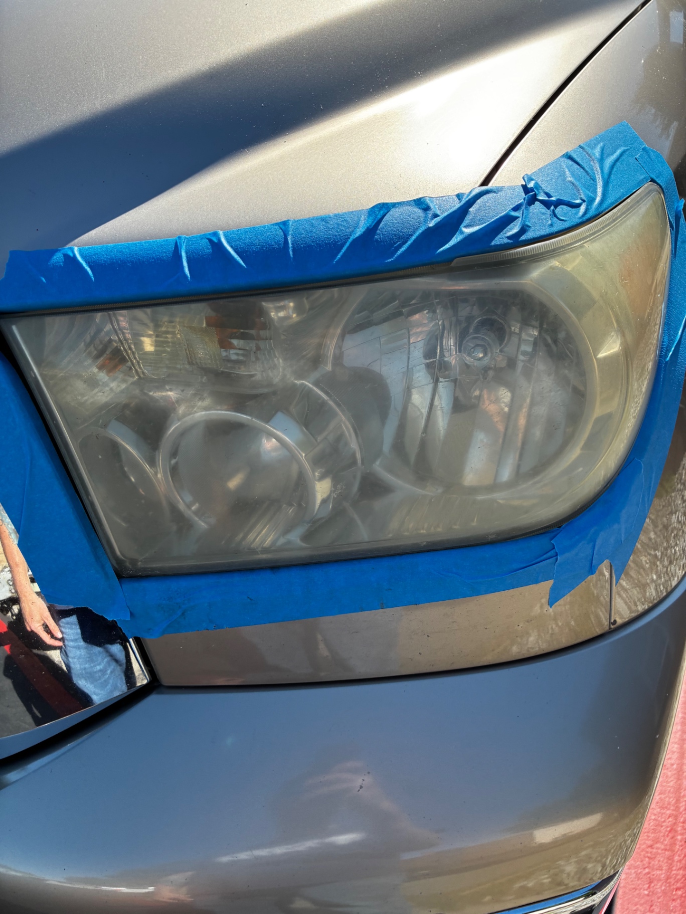 Toyota headlight before restoration — foggy, yellowed, oxidized lens masked with blue painter's tape