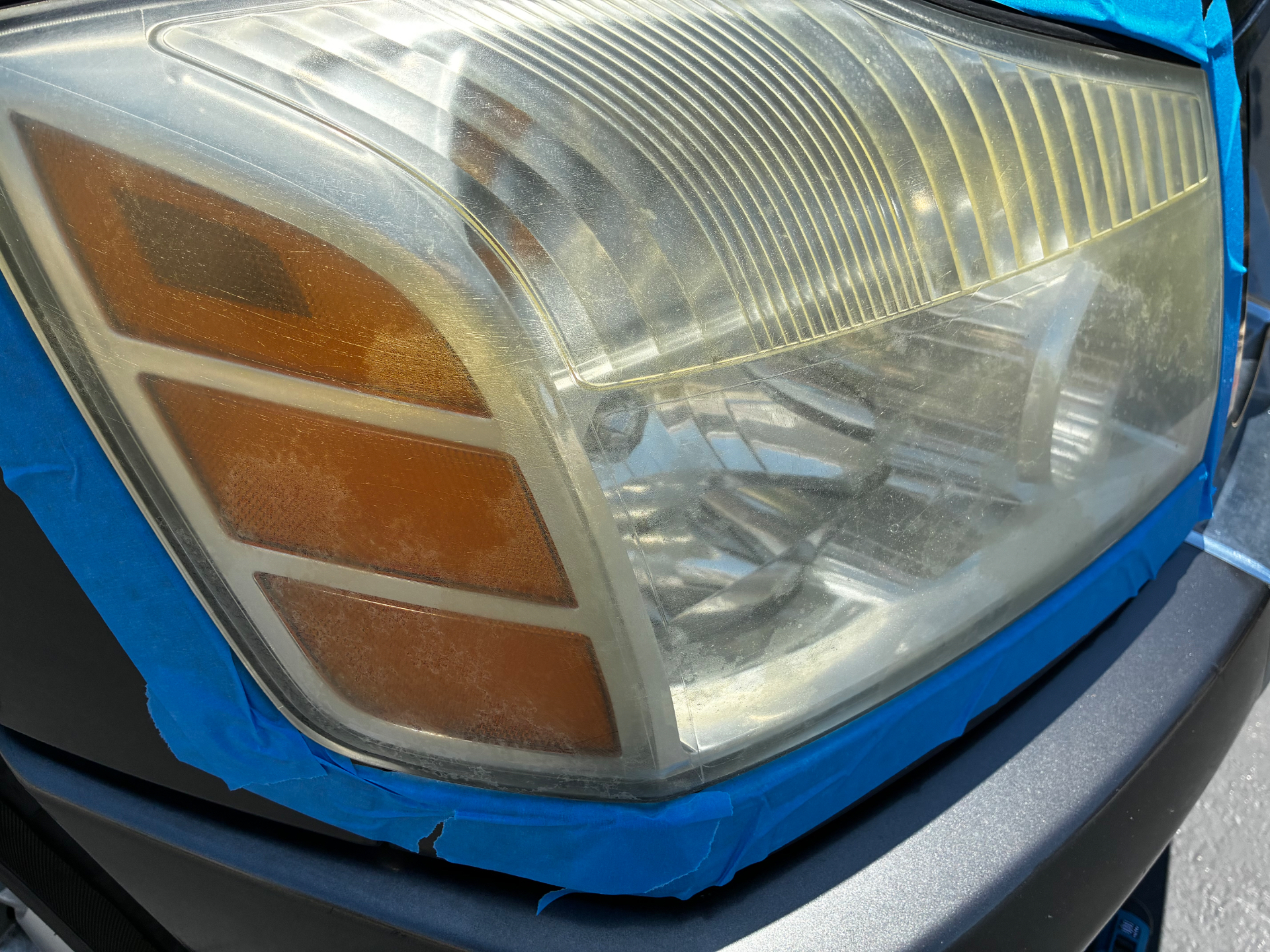 Close-up of taped-off oxidized headlight during Detail X multi-stage restoration process